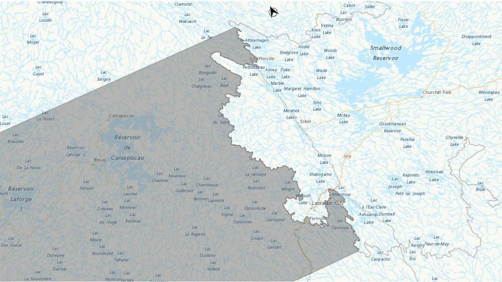 The image is a detailed map focusing on the Caniapiscau Reservoir and its surrounding areas. A large gray-shaded area dominates the left side of the map, representing the spread of smoke from nearby wildfires. The smoke covers a significant portion of the map, including the Reservoir de Caniapiscau and Reservoir Laforge. The map also features numerous labeled lakes, rivers, and reservoirs, such as Smallwood Reservoir and Churchill Falls. The border between Quebec and Labrador is marked, with the Caniapiscau region primarily situated in Quebec. The smoke overlay provides a visual indication of how the wildfires are impacting this remote, rugged area, with its dense network of water bodies and vast wilderness.